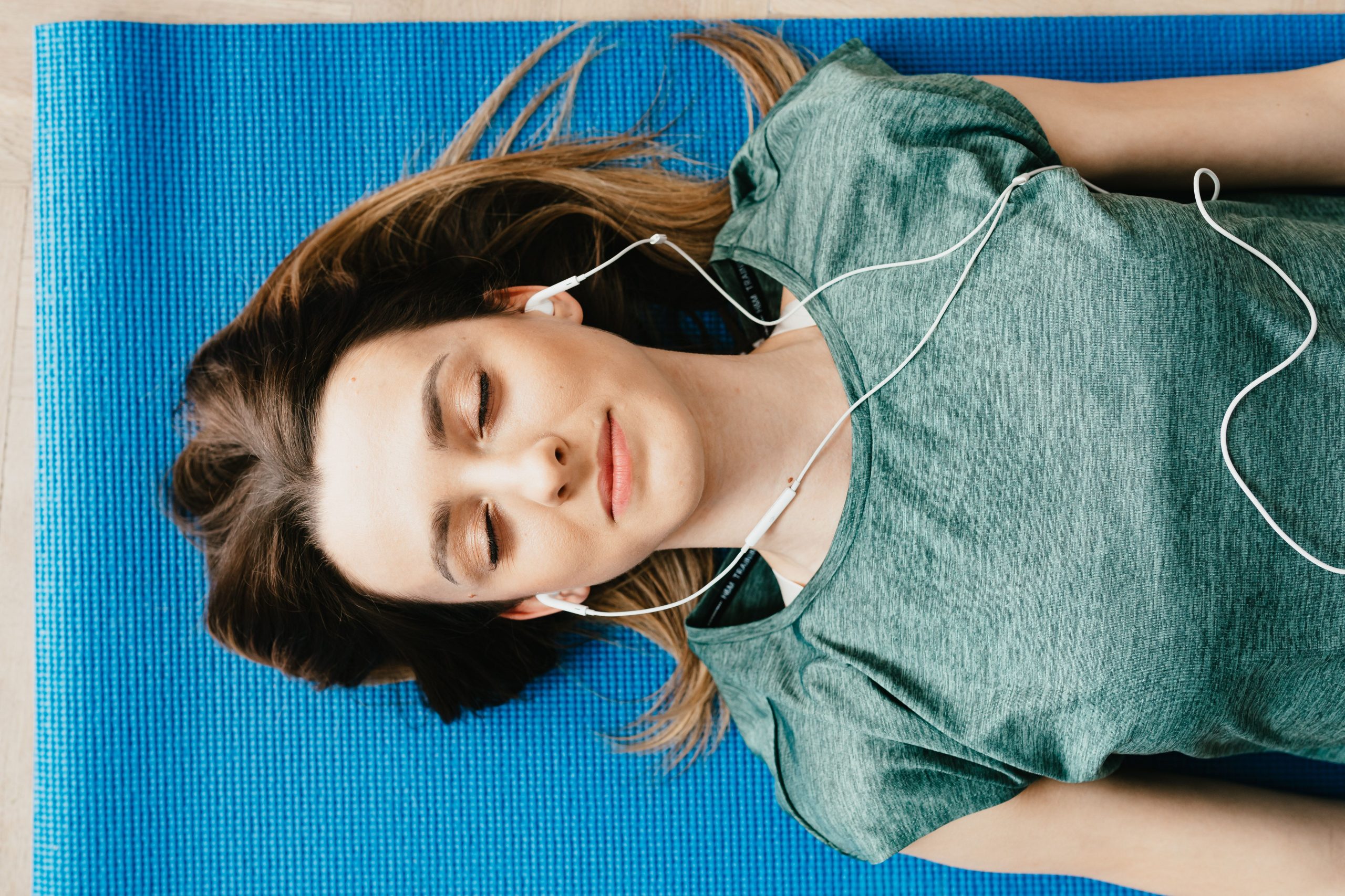 woman on a blue yoga mat meditating with wired headphones